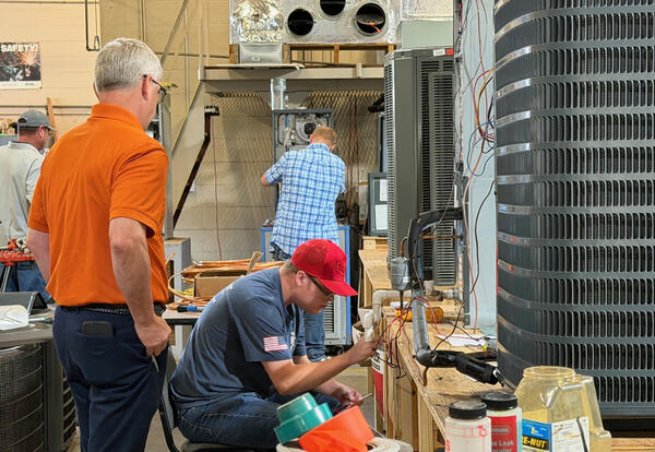 A Fletcher Technical Community College student works on HVAC equipment inside the Air Conditioning and Refrigeration lab while a regional employer observes during the Skilled Trades Recruitment Showcase. Large air conditioning units, tools, and training e
