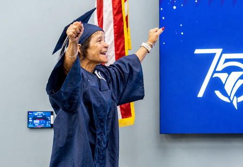 Shirley Billiot, 66, raises her arms in celebration while wearing a cap and gown before receiving her HiSET high school equivalency diploma through Fletcher Technical Community College’s WorkReady U program during a graduation ceremony.