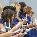A line of Practical Nursing graduates in blue scrubs hold lit nursing candles and printed programs while reciting the Nightingale Pledge during Fletcher Technical Community College’s Nursing Pinning Ceremony.