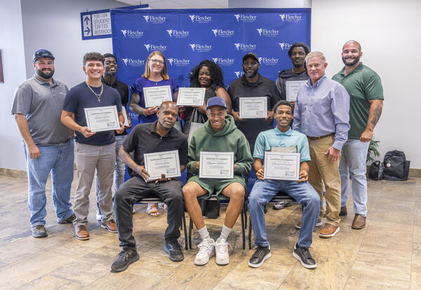 Nine Heavy Equipment Operations graduates pose with their certificates alongside three representatives of Fletcher Technical Community College and Venture Global following the Will to Skill Cohort Four graduation ceremony.