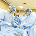 Fletcher Surgical Technology students wearing surgical gowns, masks and gloves practice a simulated procedure around an operating table in a healthcare training lab.
