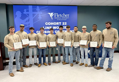 Eleven graduates of Fletcher Technical Community College’s 22nd Certified Line Worker Program cohort stand together holding their certificates during the completion ceremony on August 13, 2026.