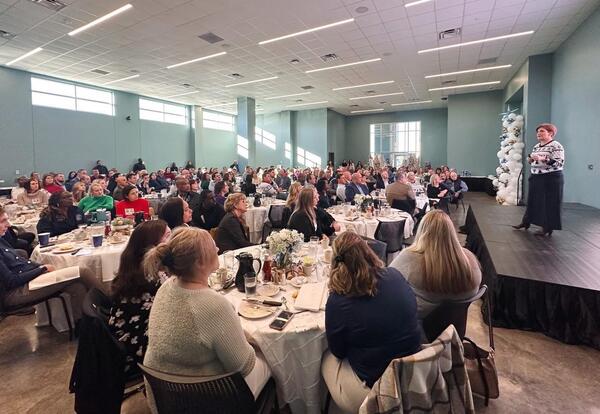 Fletcher Chancellor Dr. Kristine Strickland speaks from a stage to a large audience seated at tables during the annual Chancellor’s Breakfast.