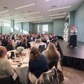 Fletcher Chancellor Dr. Kristine Strickland speaks from a stage to a large audience seated at tables during the annual Chancellor’s Breakfast.