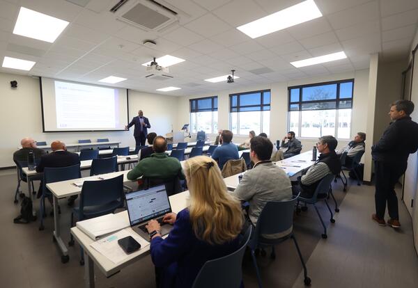 Attendees seated at classroom tables listen as Ron C. Henderson presents beside a projected slide at Fletcher Technical Community College’s Bayou Region Continuing Education Symposium.