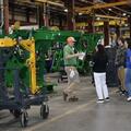 H. L. Bourgeois High School students gather around a tour guide beside green manufacturing equipment on the John Deere factory floor in Thibodaux.
