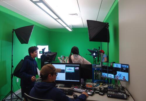 ORMS News Crew students rehearse in the studio; one student operates the computers and switchboard.