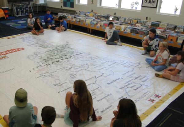 Students sitting on a library floor looking at a room sized map of NH