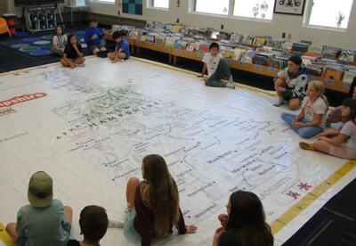 Students sitting on a library floor looking at a room sized map of NH