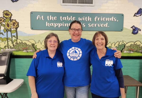 Three ladies wearing blue shirts with their arms around one another.