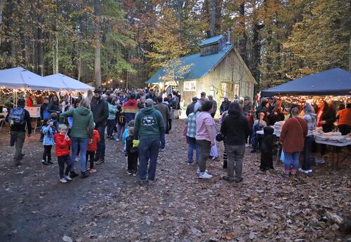A group of people gathered at night in front of the Moharimet sugar house during the 2025 Pumpkin Stroll.