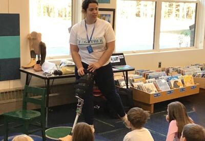Woman demonstrating the use of a prosthetic leg to a room of students