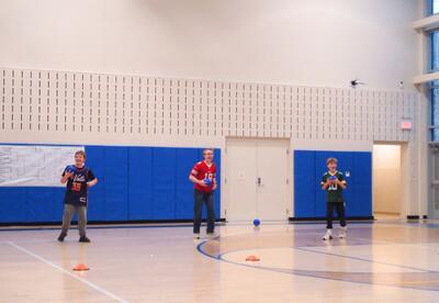 Three 8th grade students from Team Blandorians stand in the school gym holding dodgeballs during the tournament.