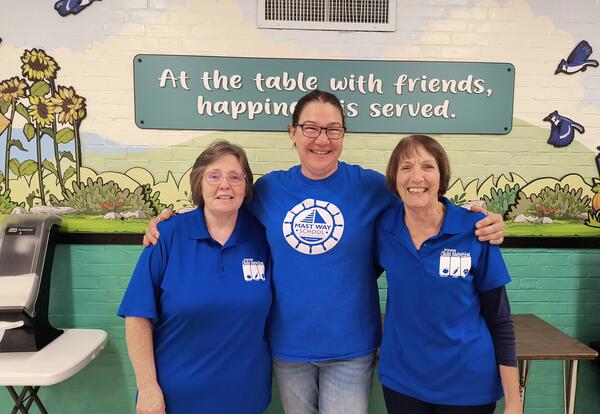 Three ladies wearing blue shirts with their arms around one another.