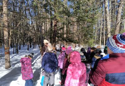 Students in snow gear gathered around a tree listening to a woman talk.