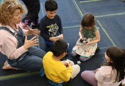 Students and a teacher sitting on a blue rug building a cube shaped robot