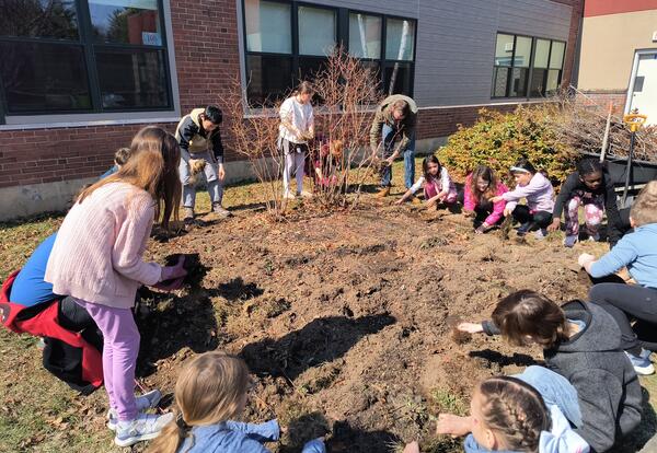Children kneeling beside a 12 X 12 square garden plot digging in the soil.