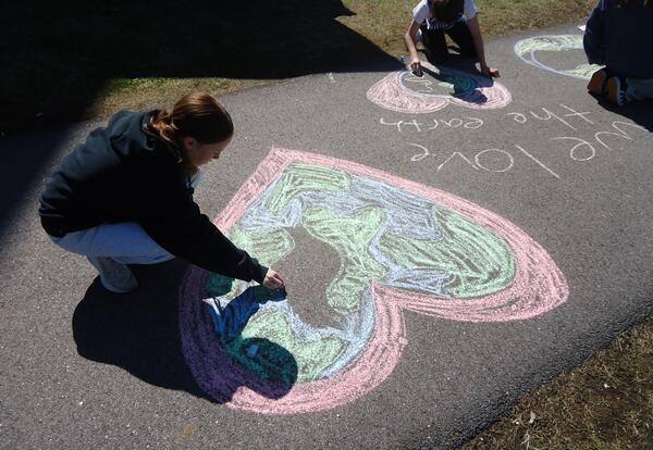Students draw and write chalk messages on the sidewalk during Earth Week.