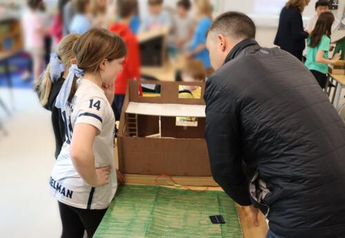 Students explaining their tiny home's sustainable features to a parent.