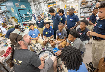 Sixth graders listen closely as instructor Jon walks them through the next step in their wheel throwing process during a full-day visit to Queen City Clay in Norwood.
