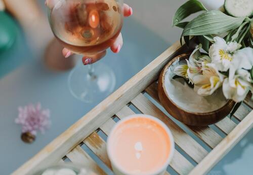 Somone sitting in a bathtub (only arm visible) holding a glass of wine with flowers and candle nearby