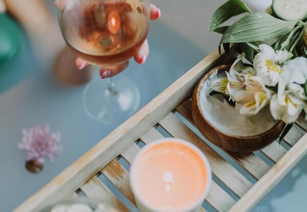 Somone sitting in a bathtub (only arm visible) holding a glass of wine with flowers and candle nearby