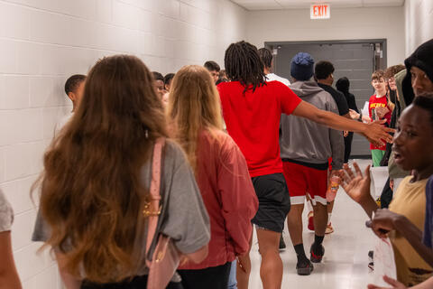 A senior student extends his arms to give high fives to underclassmen on both sides of him as he walks by. 