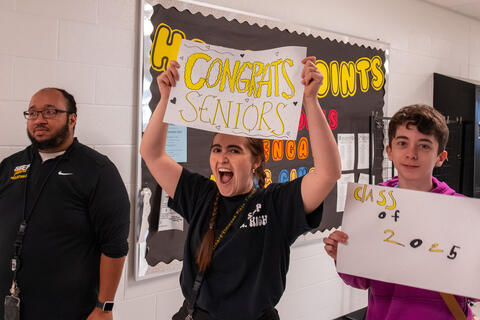 A teacher at SBEP cheers and holds up a sign that reads "congrats seniors."