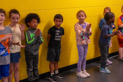 Elementary children smile and clap as senior students pass them in the hallway. 