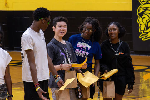 A small group of eighth-grade students smile while talking together and holding their awards.
