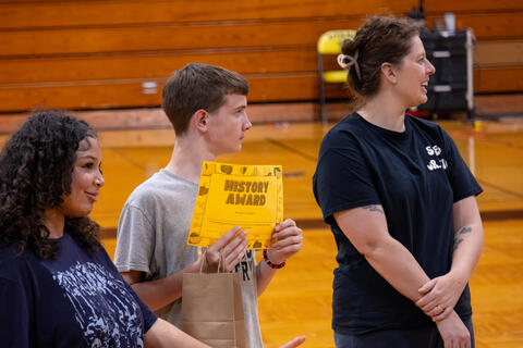 An eighth-grade student holds up an award certificate that he received. 