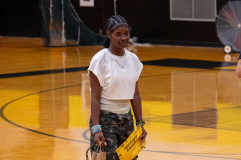 An eighth-grade student stands and looks off-camera while holding an award certificate. 