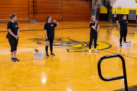 A group of teachers with microphones address the crowd on the bleachers. 