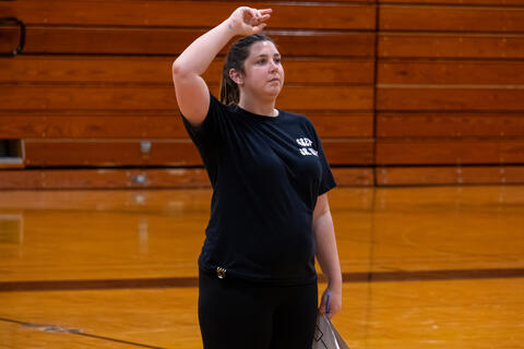 A teacher holds her hand above her head in order to give instructions. 