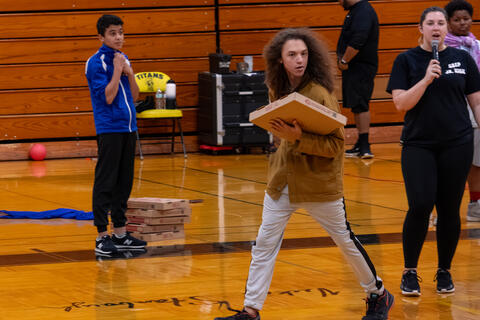 A student holding a pizza box for a game walks across the gym floor. 