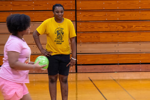 An eighth-grade student smiles on the sidelines during a game of dodgeball. 