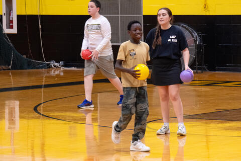 A student holding a dodgeball smiles as he walks across the floor of the Jerry Radtke Gymnasium. 