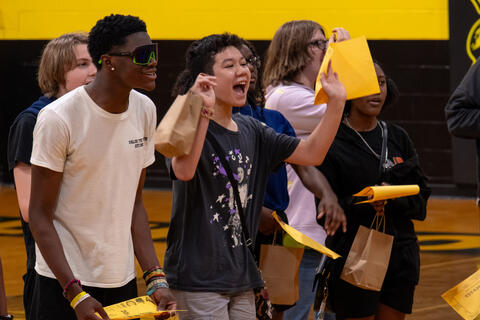 Eighth-grade students cheer while holding their award certificates. 