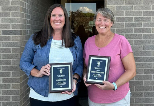 Lindsey Louis and Charnie Flynn stand together, holding up their SBEP Education Hall of Fame plaques.