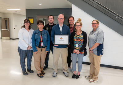High school staff stand together for a picture while holding a 2025 Momentum Award.