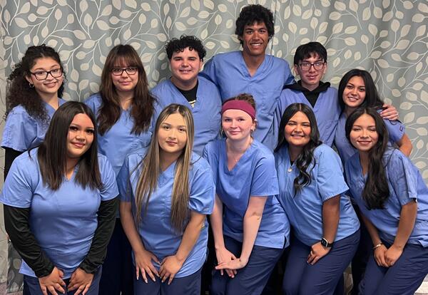 Students in scrubs pose for a photo in a clinic