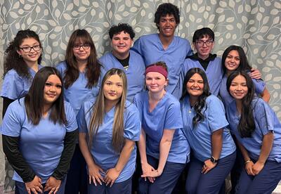 Students in scrubs pose for a photo in a clinic