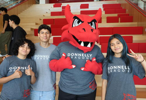 Three Donnelly students stand with Lux, the dragon that serves as Donnelly's official mascot.
