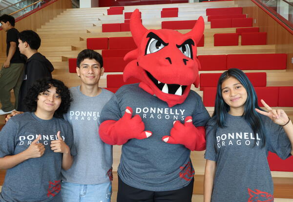 Three Donnelly students stand with Lux, the dragon that serves as Donnelly's official mascot.