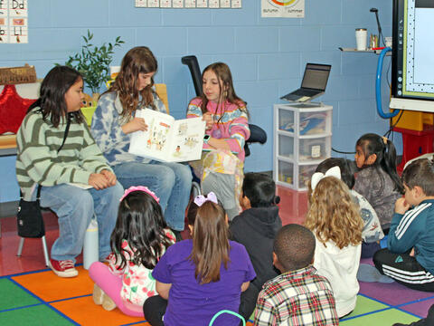photo of big kid students read to little kid students
